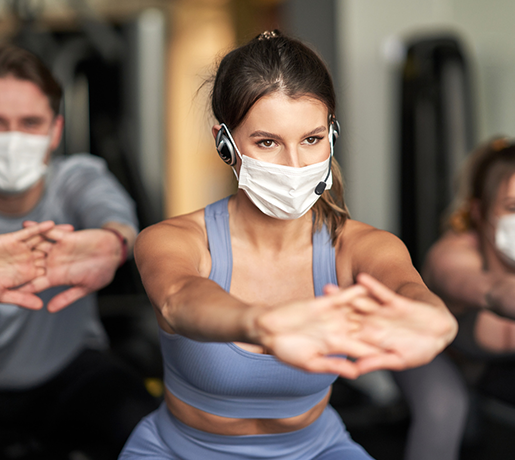group exercise class instructor with mask, demonstrating squat with arm stretch